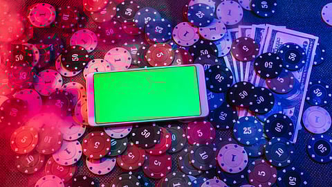 Smartphone with green screen among poker chips and dollar bills on a casino table