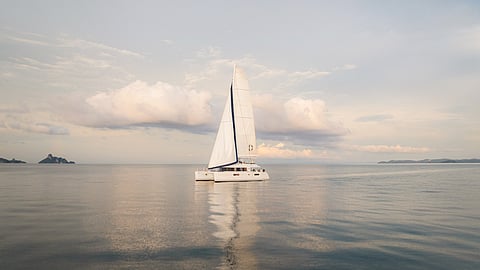 Luxury catamaran with full sails on calm ocean at sunset