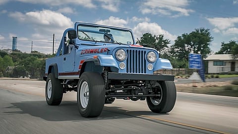Vintage-inspired Jeep Scrambler driving on road with open top and rugged stance
