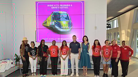 Group of students and officials posing in front of Brightline display screen inside station