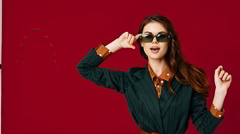 Woman in green outfit posing with sunglasses against red background