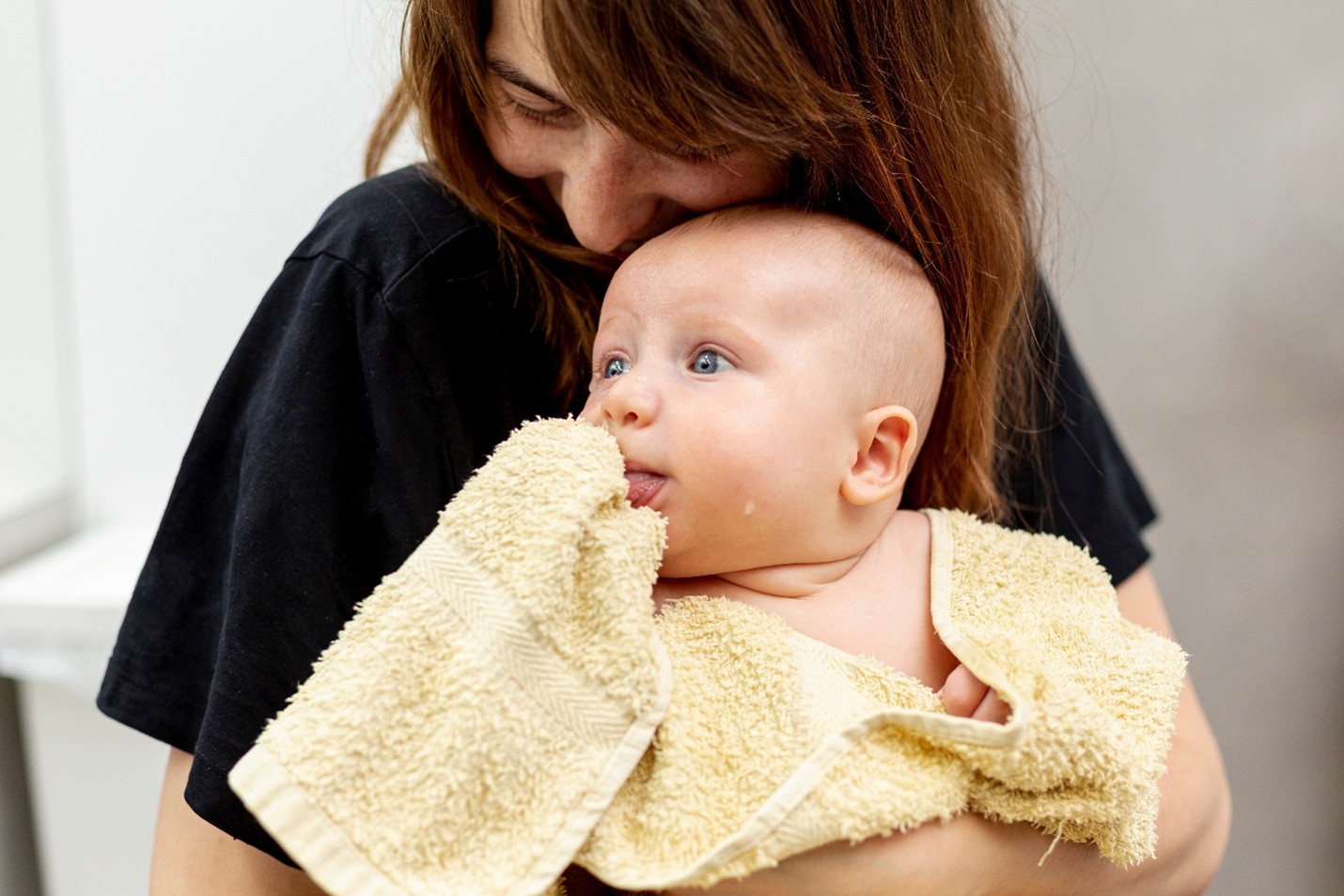 A person holding a baby wrapped in a yellow towel.