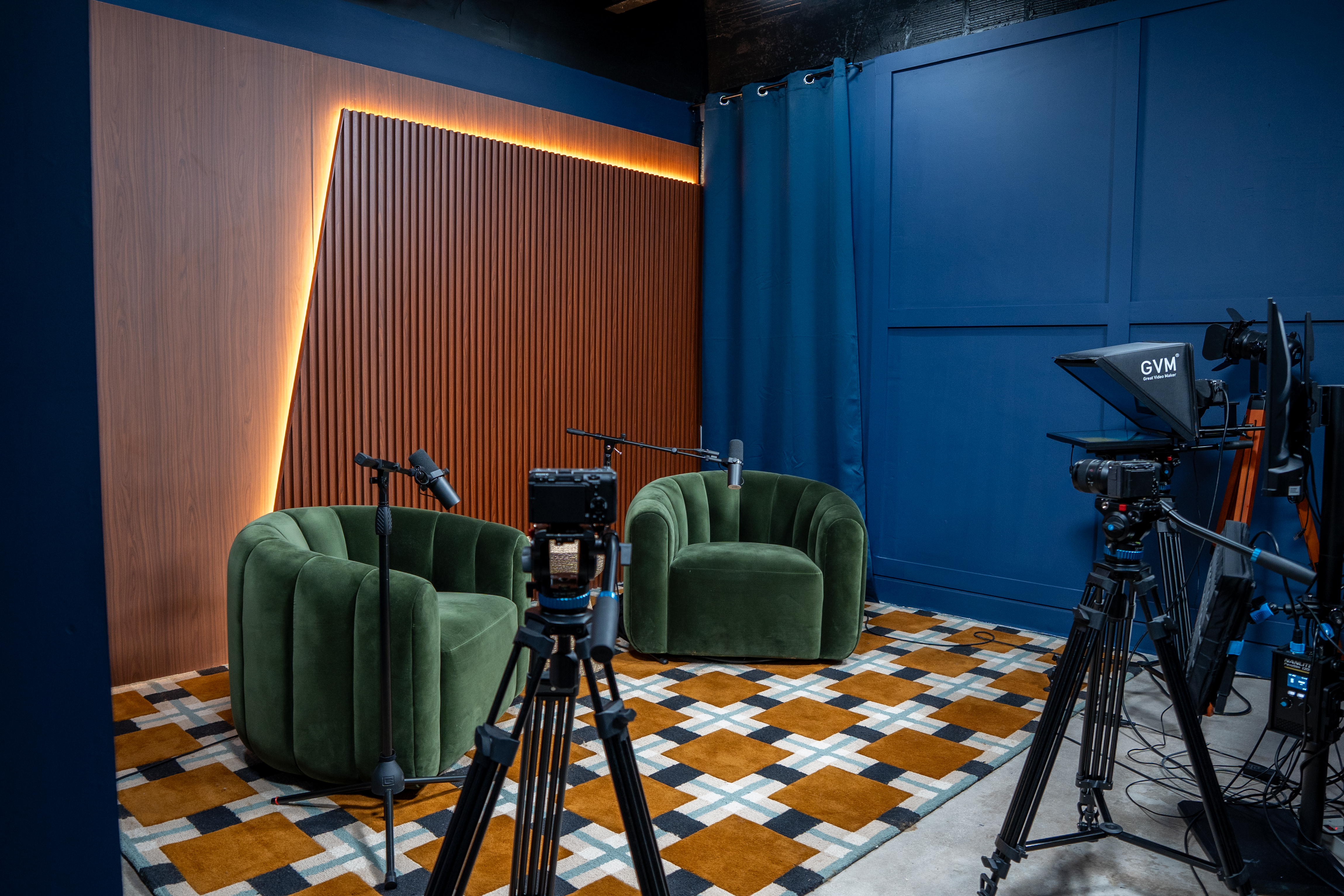 Podcast studio with green chairs, cameras, and microphones set for recording
