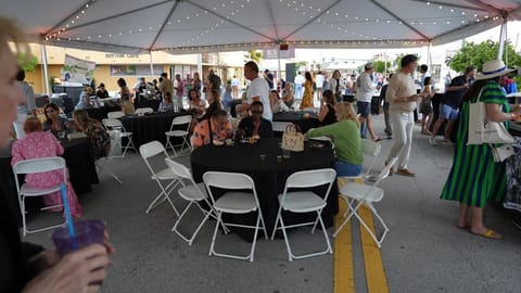Guests seated at tables enjoying food and drinks under a large outdoor event tent