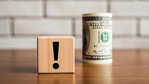 Wooden block with exclamation mark beside rolled cash