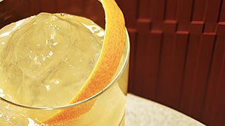 Close-up of a Gold Rush whisky cocktail with orange peel garnish over ice