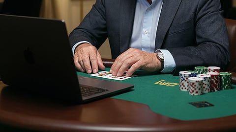a man focused on a computer screen while seated at a green poker table
