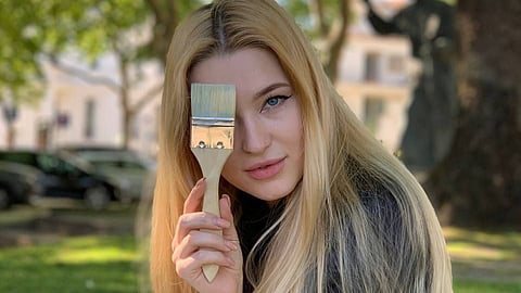 Kateryna Mariien holding a paintbrush outdoors in a park setting