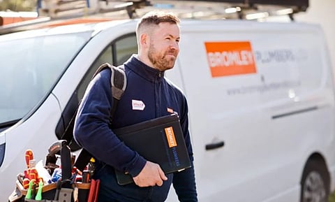 a professional plumber carrying tools and a clipboard next to a company van