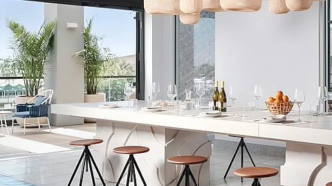 Long white communal table with stools, wine glasses and pendant lights at Olive & Sea