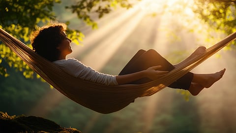 Person relaxing in a hammock beneath sunlit trees during a peaceful moment outdoors