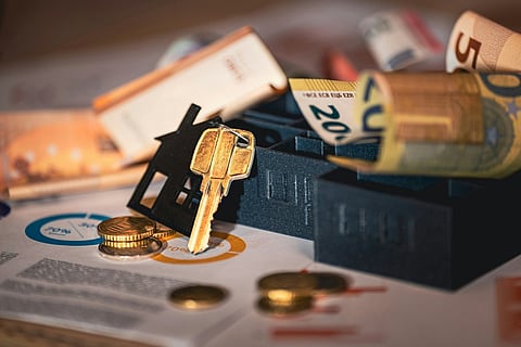 Euro currency notes, coins, and a house key laid out over financial charts