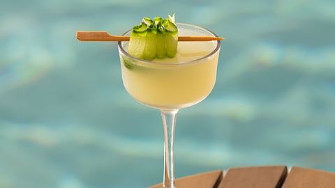 Cucumber & Basil martini with cucumber ribbon garnish beside a pool