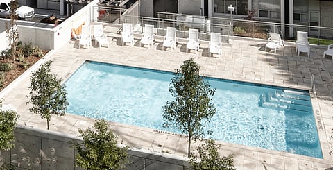 a light-colored stone deck with multiple white lounge chairs and modern landscaping