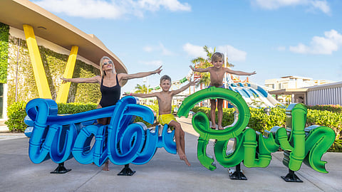 Family posing at Palace Elite resort entrance with children near a colorful welcome sign