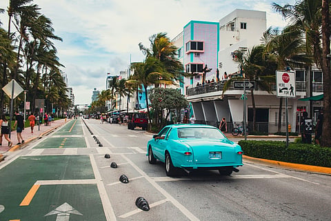 a turquoise blue Ford Thunderbird driving down Ocean Drive in Miami Beach