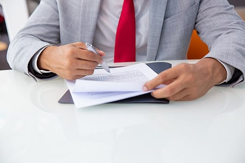 a professional in a grey suit and red tie signing a document