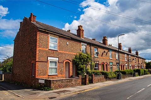 Row of red brick terraced houses along a street under a partly cloudy sky.
