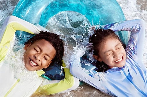 Two girls in wetsuits riding inflatable rafts through incoming waves at the beach.