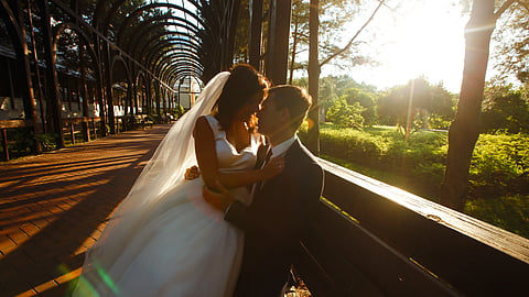 Bride and groom embracing beneath a garden walkway at sunset