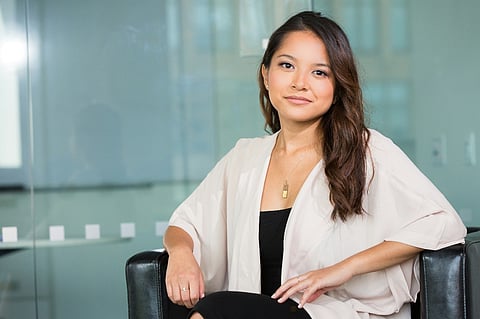 Woman in a cream cardigan smiling in a modern glass office.