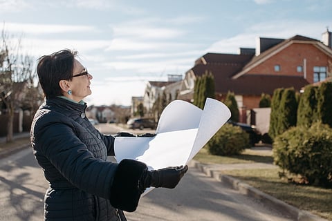 Person holding architectural plans outdoors in a residential neighborhood