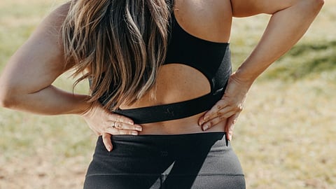 Person wearing black sportswear with hands on lower back outdoors.