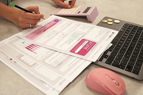 Person reviewing financial documents with a laptop, calculator, and coins on a desk.