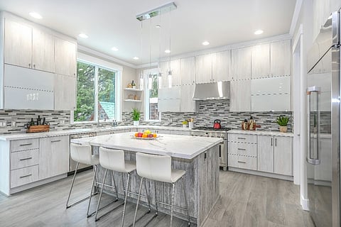 Modern white kitchen with marble island, cabinets, and bar seating.