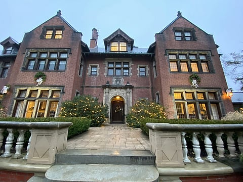 Historic brick mansion with illuminated windows, landscaped entrance, and stone pathway.