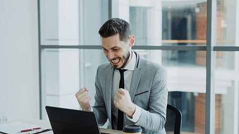 Businessman celebrating success while working on a laptop in an office