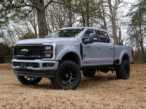 Silver pickup truck with off-road tires parked in a wooded outdoor area