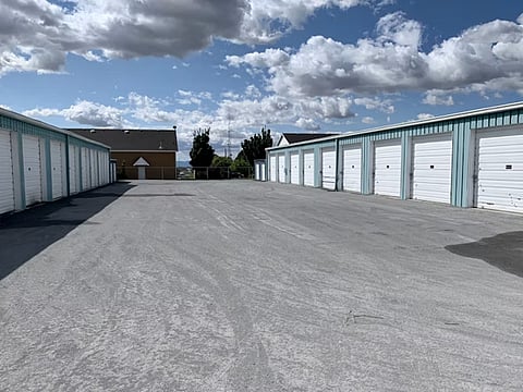 Storage facility with multiple garage units and a large paved lot under a cloudy sky