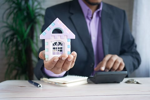Real estate professional holding a model house while calculating finances
