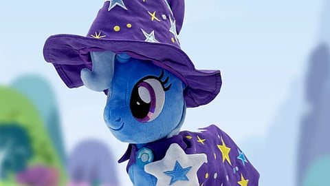 Blue plush toy character wearing a purple wizard hat and star-patterned cape