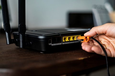 Hand connecting an Ethernet cable to a wireless router on a desk