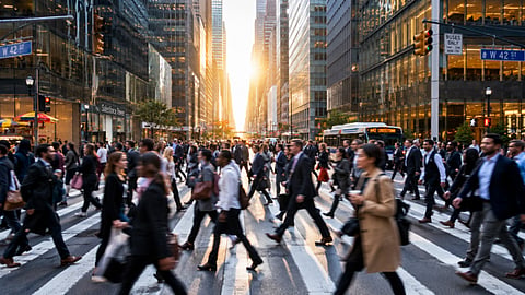 Crowds crossing a busy city street at sunset.