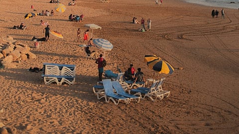 People relaxing on a sandy beach beside coastal buildings.