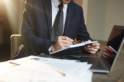 A businessman in a dark suit writes in a notebook 