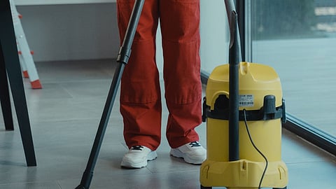 Cleaner in red overalls holding a vacuum in a modern room