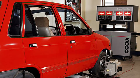 Red car undergoing computerized wheel alignment in a workshop.