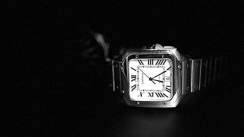 Black-and-white close-up of a Cartier wristwatch against a dark background.