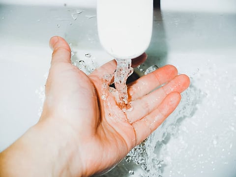 Hand washing under running water from a faucet in a clean sink.