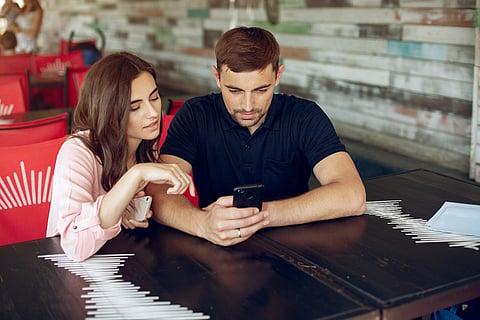 Couple sitting at a restaurant table looking at a smartphone together.