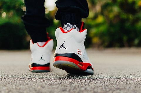 Close-up of a person walking outdoors in white, red, and black sneakers.