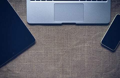 Laptop, tablet, and smartphone arranged on a textured desk.