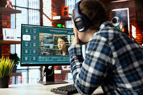 A man with headphones looking at an AI interface on a computer monitor.