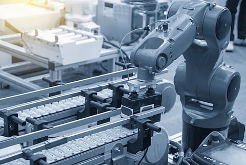 blue industrial robotic arm working with a component on a manufacturing assembly line conveyor belt.