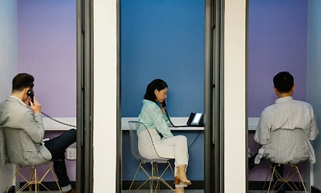 Three people making calls in office phone booths.