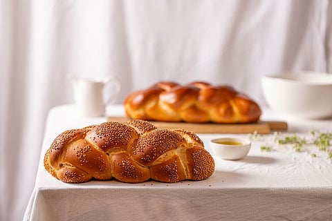 Braided challah loaf on a linen-covered table set with honey and butter